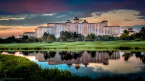 A large hotel with multiple towers, a well-maintained lawn, and a reflective water body in front. - Rosen Shingle Creek (Orlando)