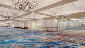 Un hall d’hôtel spacieux, doté d’un tapis à motifs, de plusieurs lustres et d’espaces aménagés pour s’asseoir.
