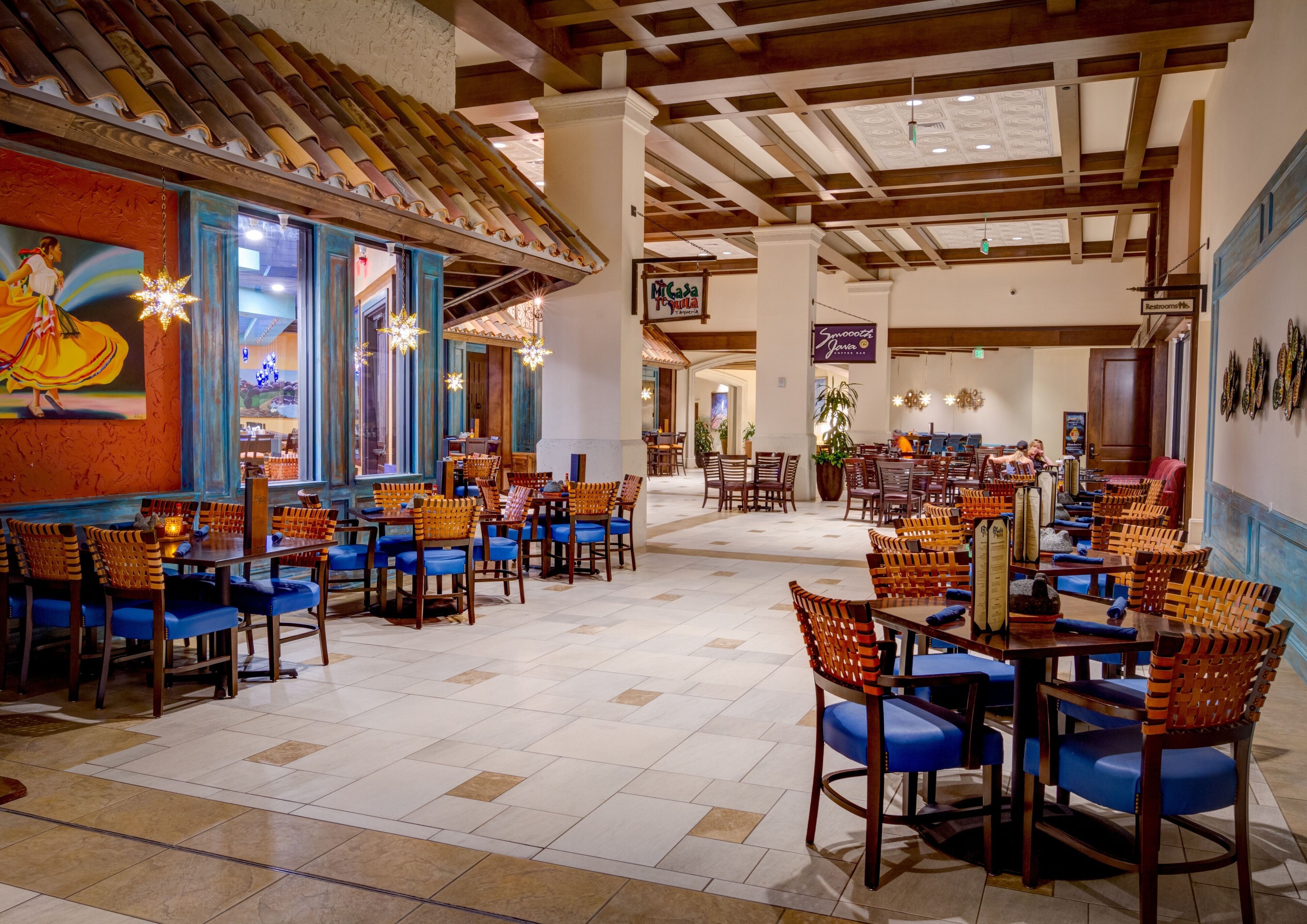 A spacious restaurant with high ceilings, exposed beams, and a mix of wooden and tiled flooring.