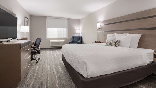 A hotel room with a bed, a desk with a computer, a chair, a TV, and a window with blinds.
