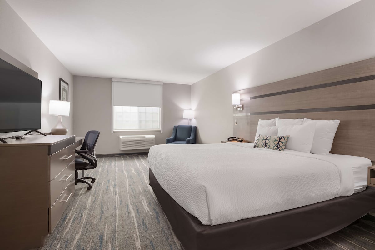 A hotel room with a bed, a desk with a computer, a chair, a TV, and a window with blinds.