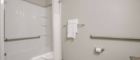 A bathroom with a bathtub, shower, toilet, and handrails.