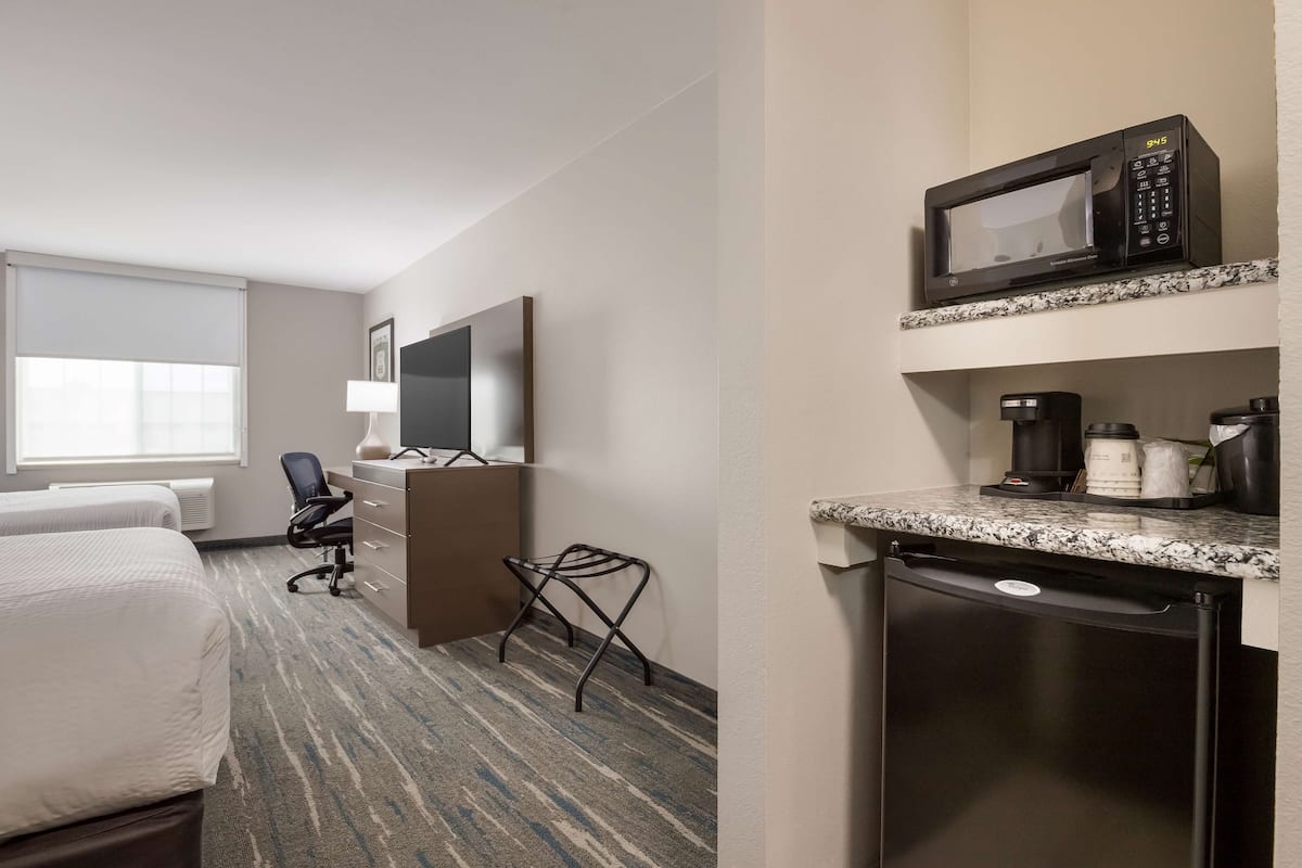 A hotel room with a bed, a desk with a chair, a microwave, a coffee maker, and a dishwasher.