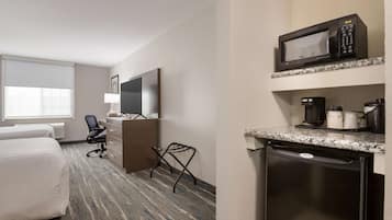 Habitación de hotel con cama, escritorio y silla, microondas, cafetera y lavavajillas.