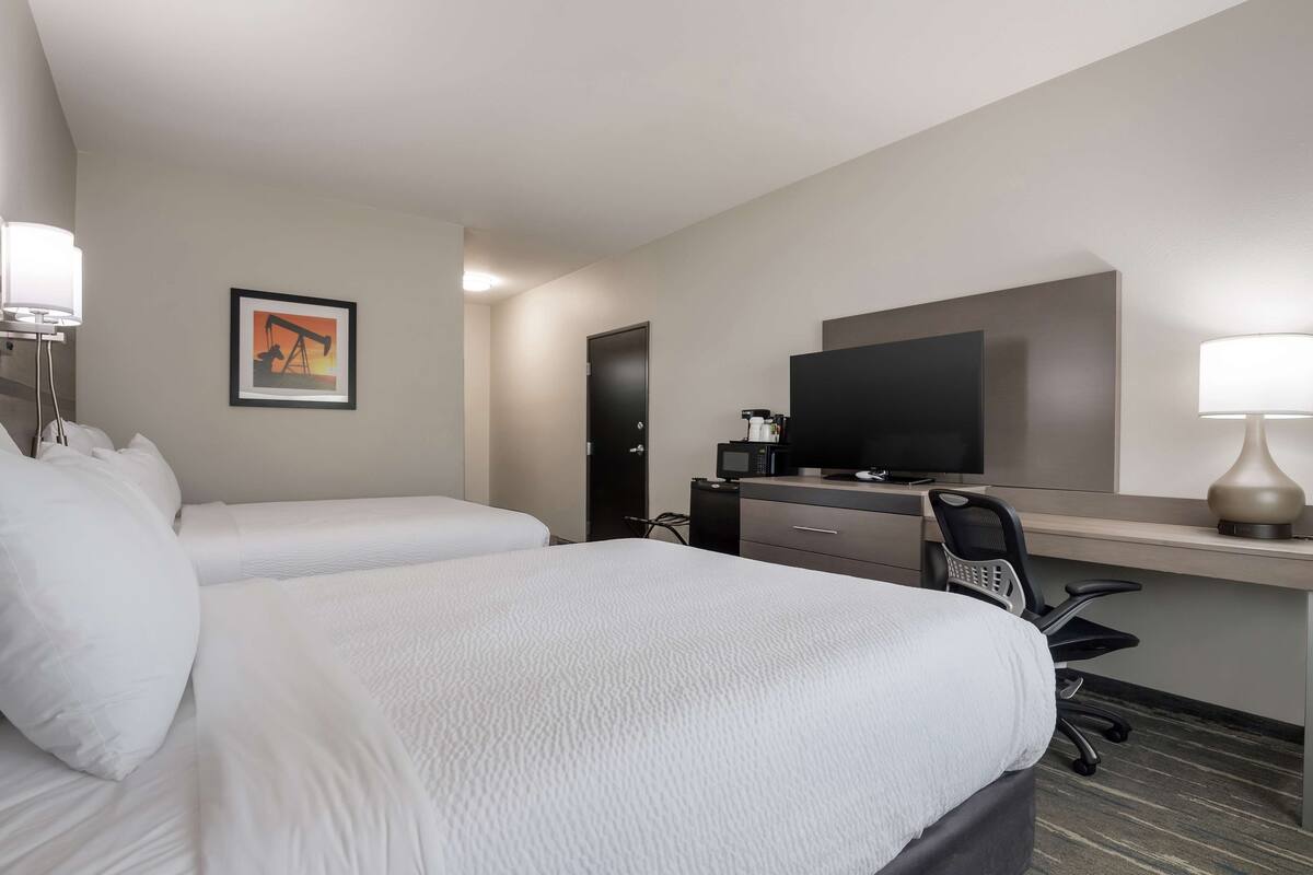 A hotel room with two beds, a desk with a computer, a television, and a lamp.