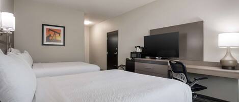 A hotel room with two beds, a desk with a computer, a television, and a lamp.