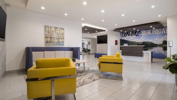 A modern lobby with yellow sofas, a reception desk, and a mural of a landscape. - Best Western NSU Inn (Tahlequah)