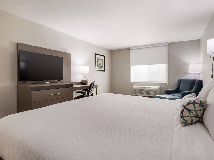 Une chambre d’hôtel avec un grand lit, un téléviseur à écran plat, un bureau avec une chaise et deux lampes.