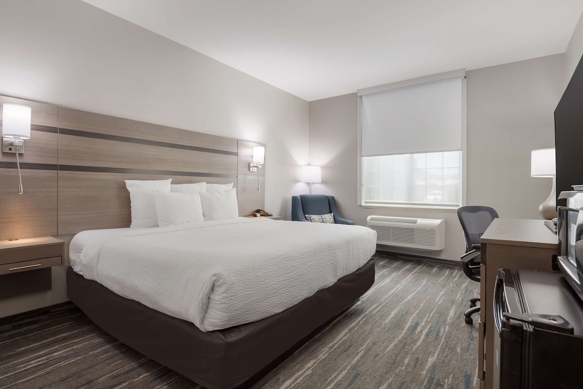 A hotel room with a large bed, bedside tables, a desk with a chair, a TV, and a window with blinds.