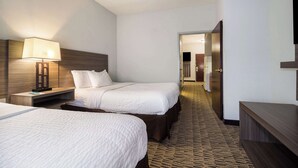 A hotel room with two beds, a nightstand with a lamp, a wooden headboard, and a carpeted floor.