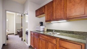 A hotel kitchen with wooden cabinets, a granite countertop, a microwave, and a coffee maker.