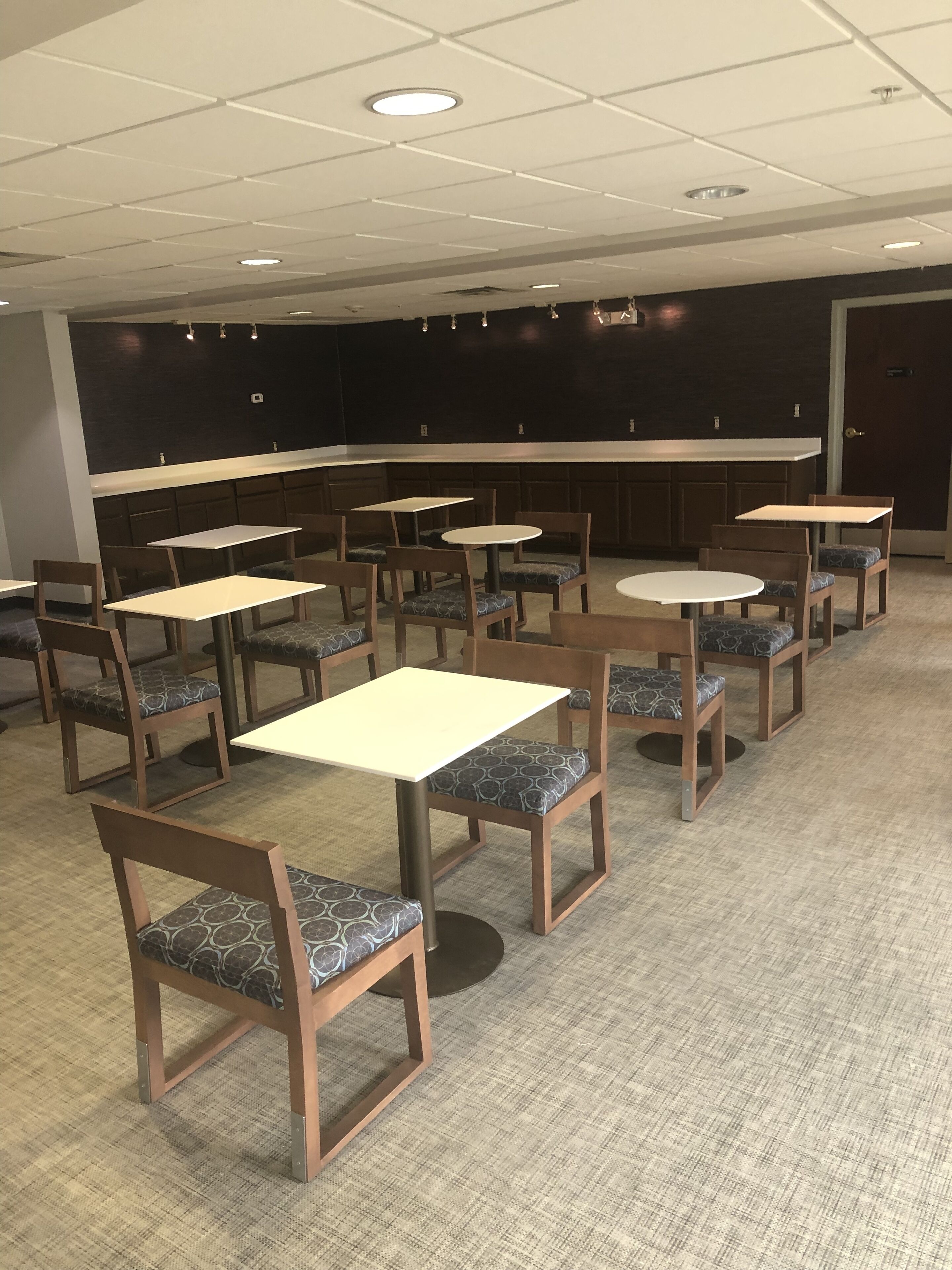 Una sala de conferencias con varias mesas y sillas, una pared de color oscuro y un techo blanco con iluminación empotrada.