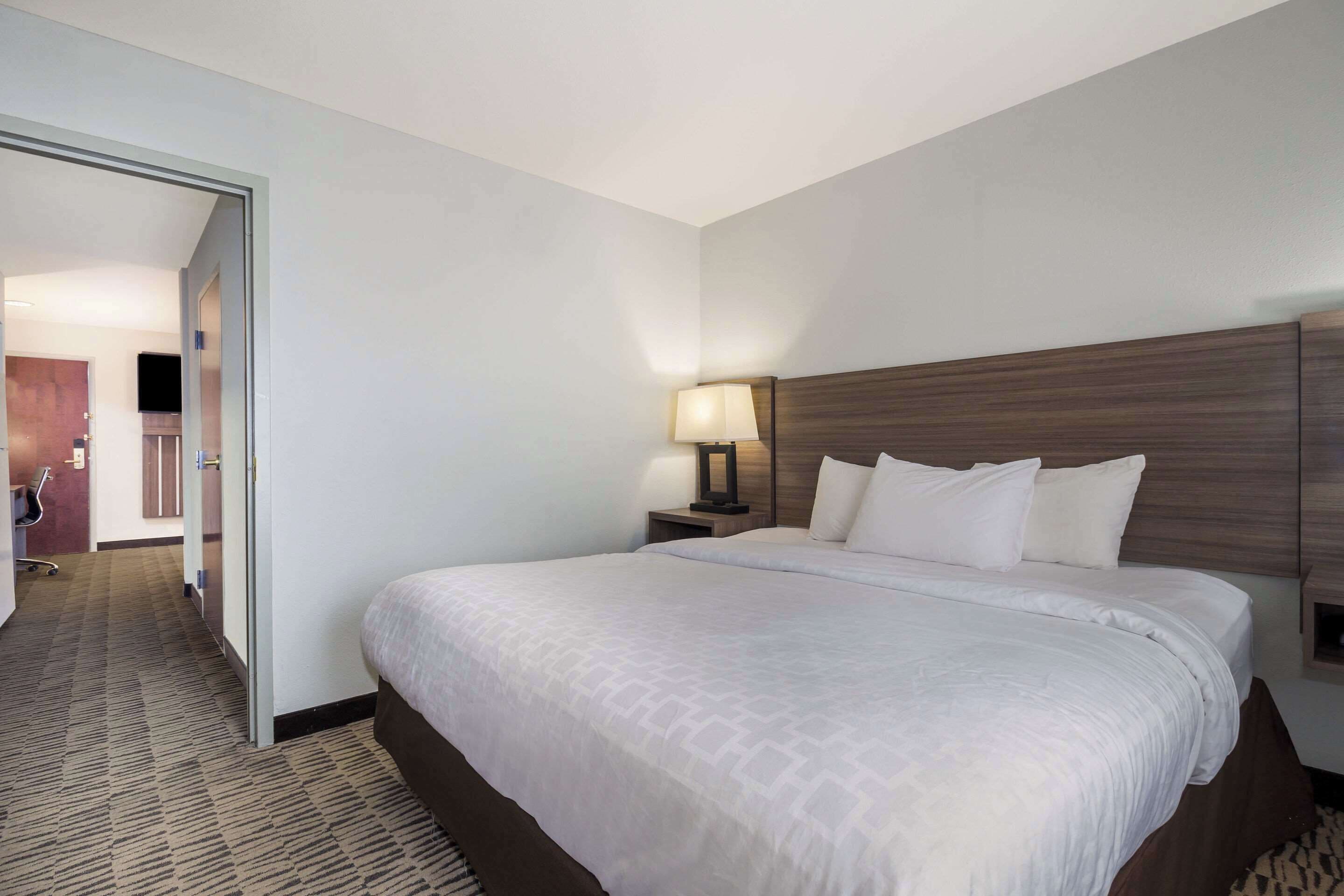 A hotel room with a large bed, a nightstand with a lamp, and a door leading to a bathroom.