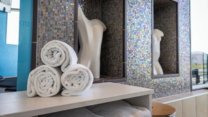 Un baño con pared de mosaicos, una bañera blanca y toallas enrolladas sobre una encimera.