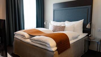 Una cama bien hecha con colcha marrón, almohadas blancas y cabecera oscura en una habitación de hotel.