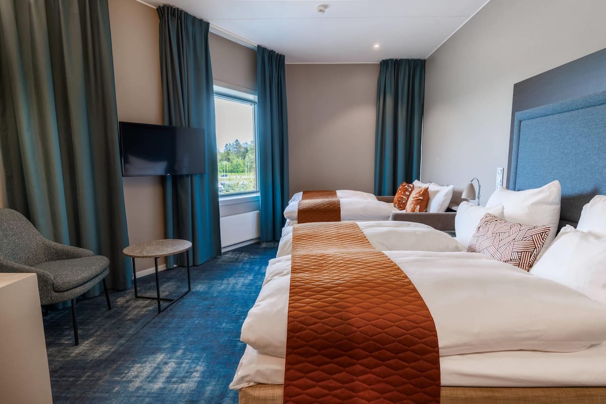Habitación de hotel con una cama grande, una mesita, una silla y un televisor.