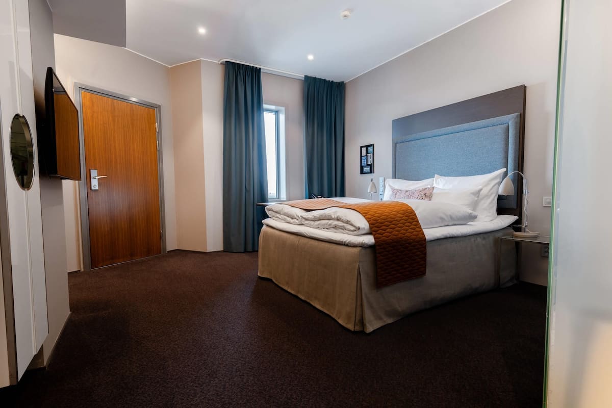 Una habitación de hotel con una cama, una mesita de noche, una lámpara y una puerta.