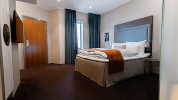 Quarto de hotel com cama, mesa de cabeceira, abajur e porta.