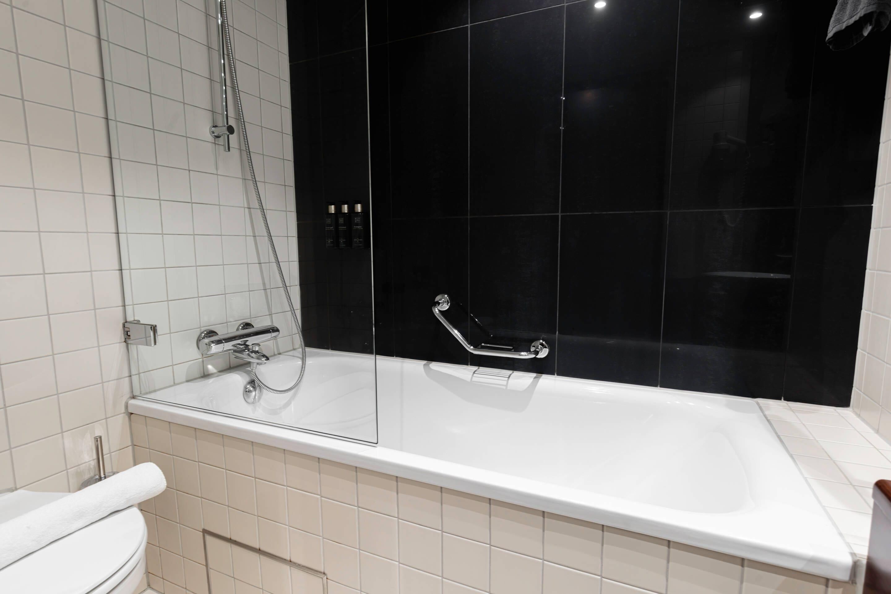 Moderni kylpyhuone, jossa on valkoinen kylpyamme, lasiseinällä varustettu suihku ja wc.