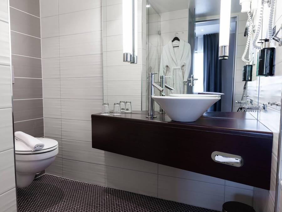 A modern bathroom with a white toilet, a dark vanity with a sink, and a mirror.