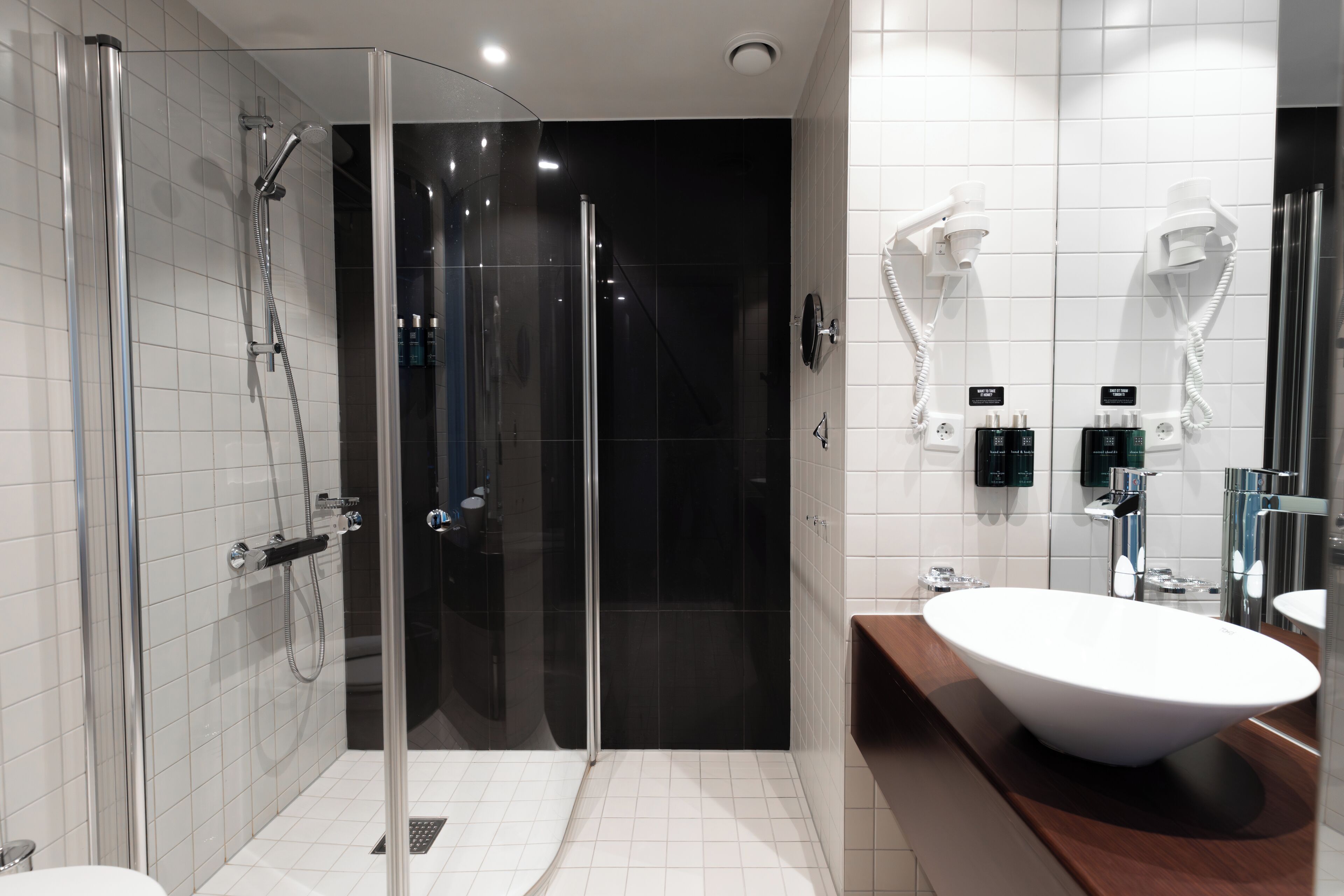 Un baño moderno con ducha de vidrio, lavamanos blanco y tocador con espejo.