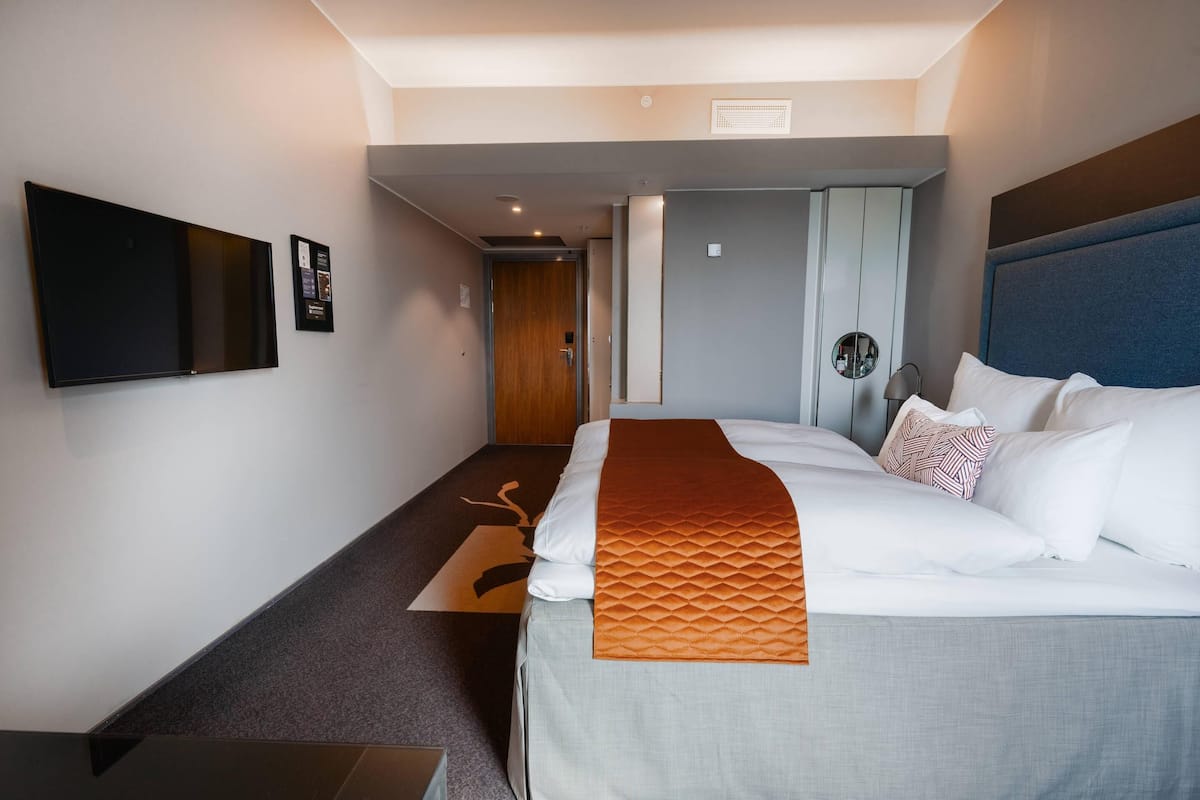 Habitación de hotel con una cama grande, un televisor de pantalla plana en la pared, una mesita de noche y una puerta que da a otra habitación.