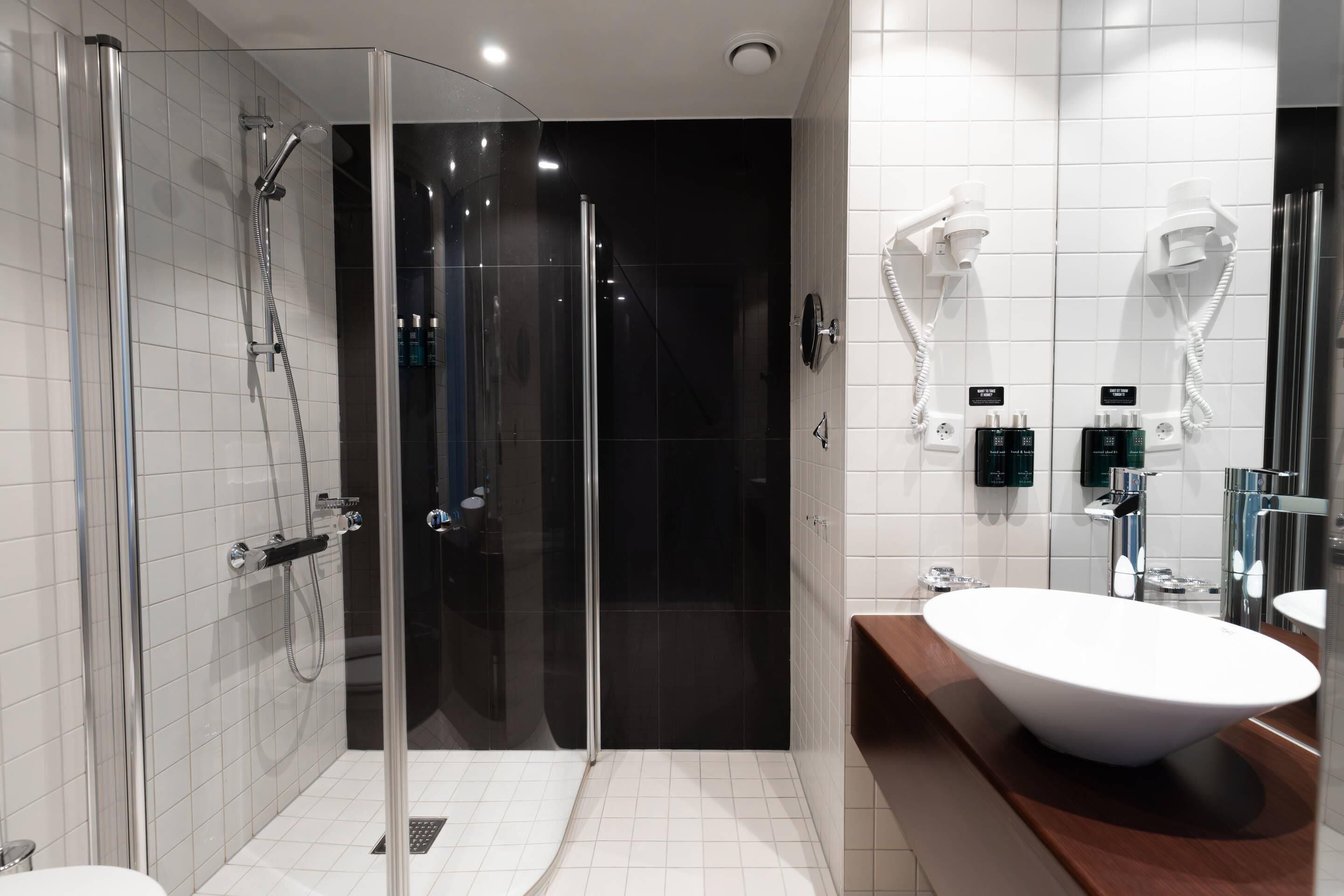 Un baño moderno con ducha de vidrio, un lavamanos grande y blanco, y una zona de ducha oscura.