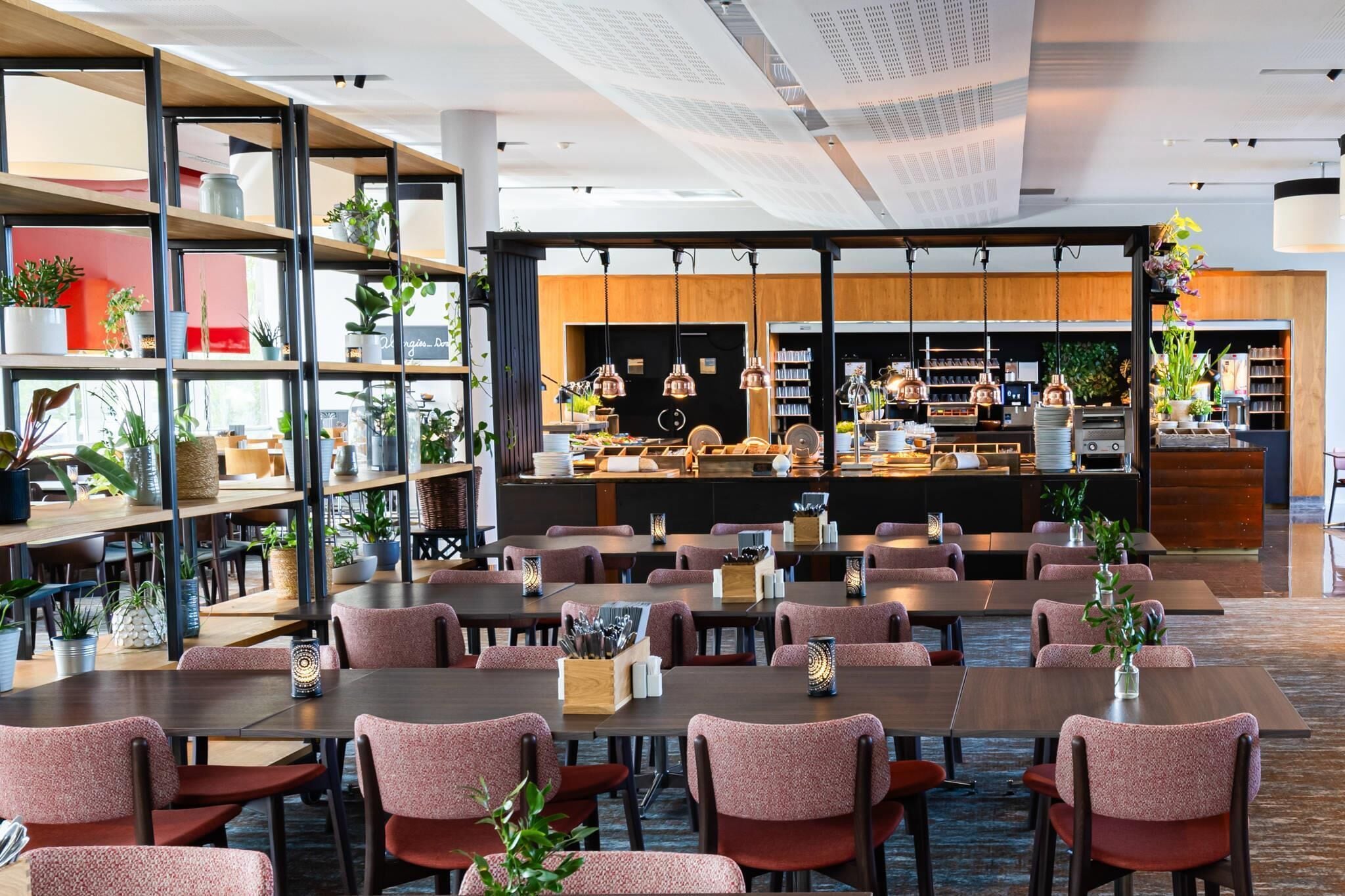 Un restaurante moderno con varias mesas y sillas, una zona de cocina y estantes con plantas.