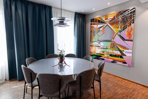 A modern dining area with a round table, six chairs, and a large abstract painting on the wall.