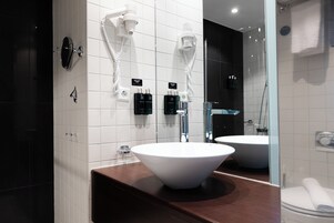 Un baño moderno con un lavamanos grande de color blanco, una bañera oscura y un espejo que refleja el ambiente.