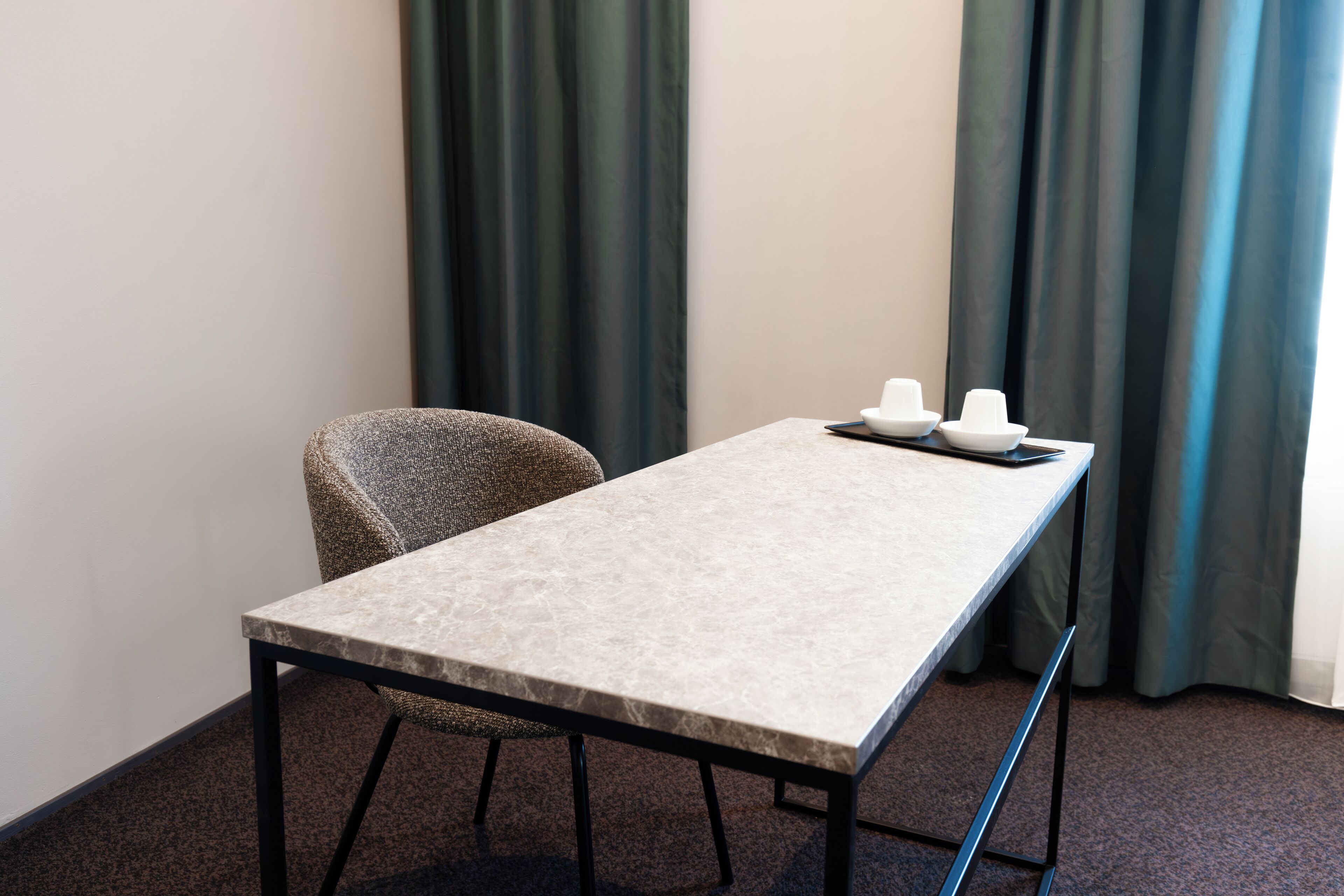 A small, neatly arranged room with a single table, a chair, and a pair of white hats on the table.