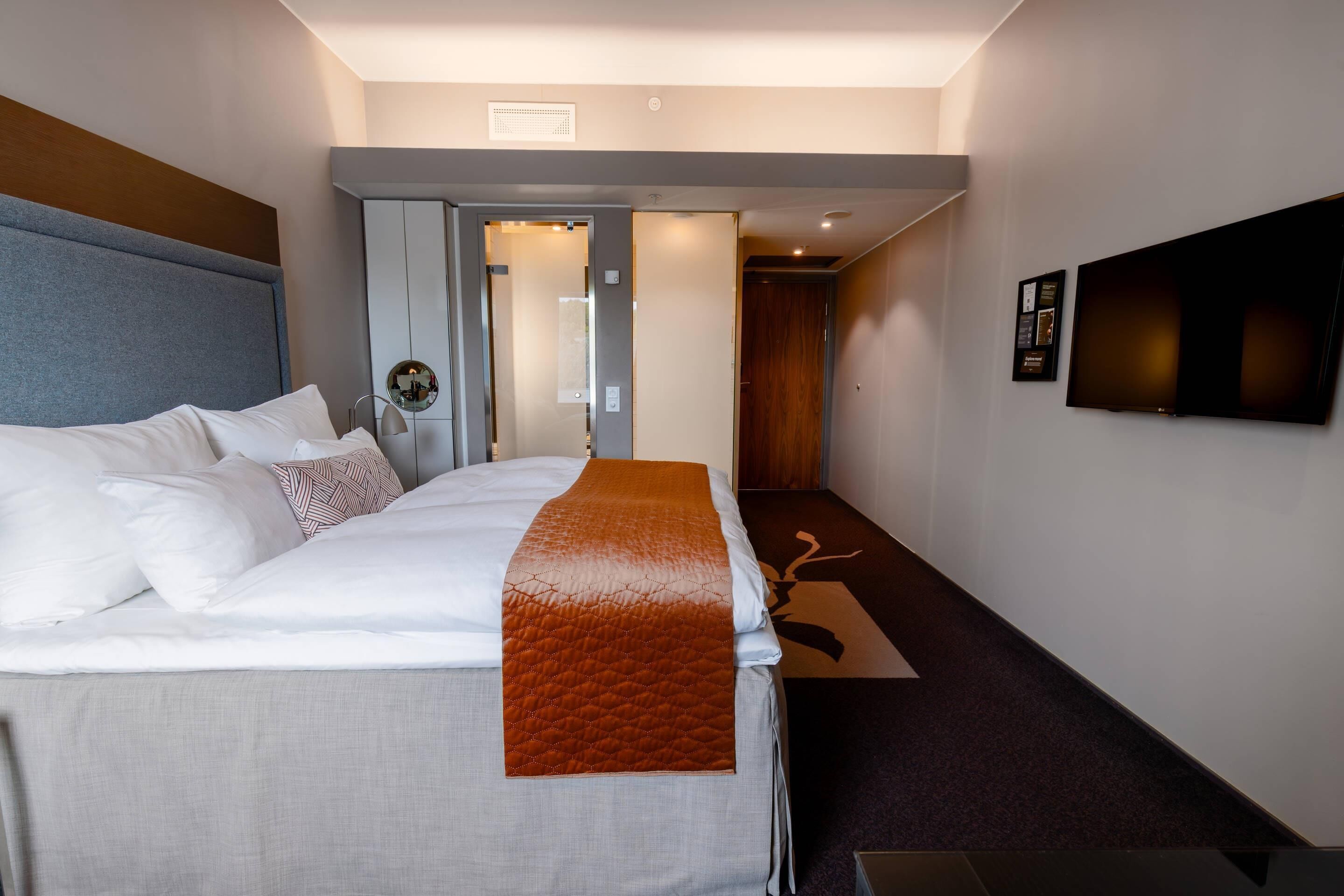 A hotel room with a bed, a flat-screen TV, a door, and a carpeted floor.