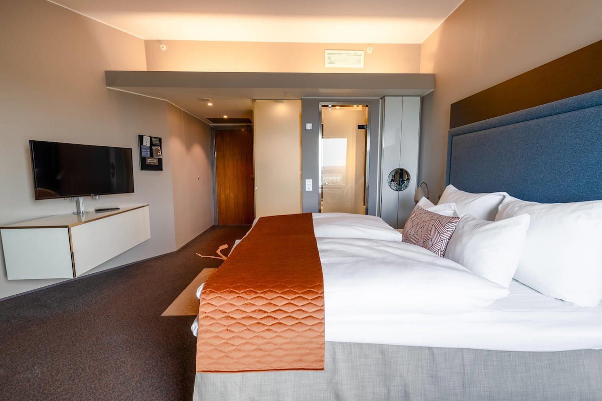 Una habitación de hotel moderna con una cama grande, un televisor de pantalla plana, un escritorio y vistas a la ciudad.