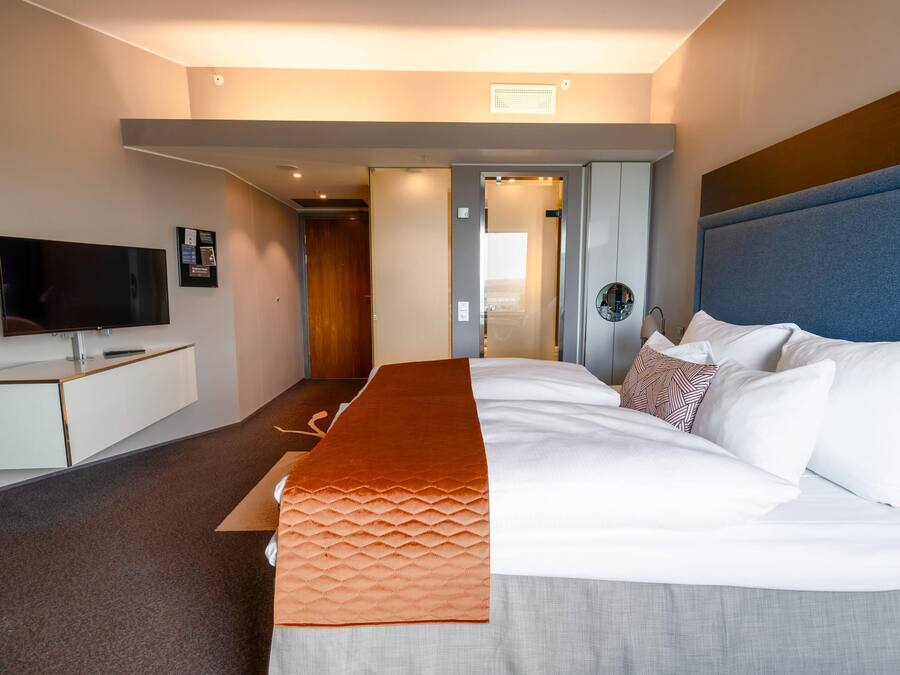 Una habitación de hotel moderna con una cama grande, un televisor de pantalla plana, un escritorio y vistas a la ciudad.