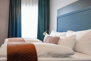 Una cama bien hecha con ropa de cama blanca y marrón, un cabecero azul y cortinas turquesa.