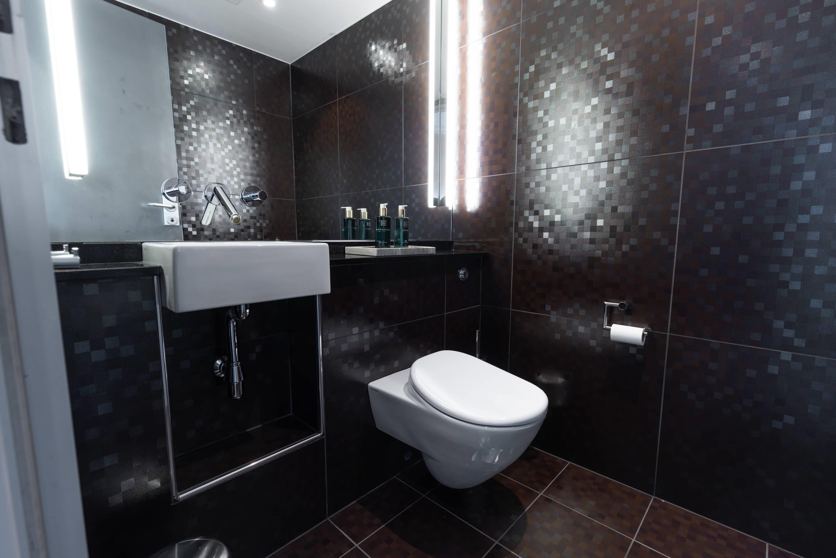 A modern bathroom with a white toilet, a sink with a mirror, and a shower area.