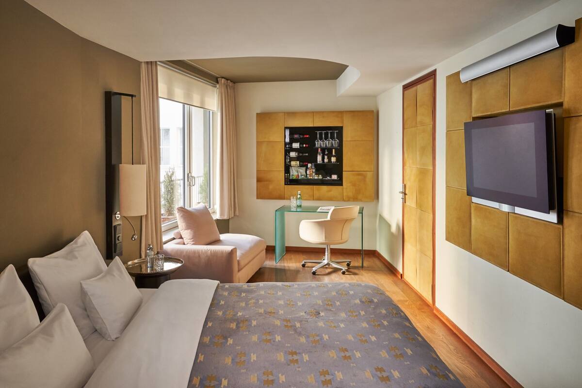 A hotel room with a bed, a desk, a chair, a TV, a minibar, and a window with curtains.