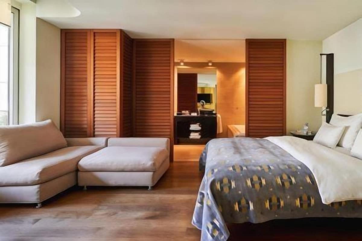 A hotel room with a bed, a sofa, a desk, and a mirror.