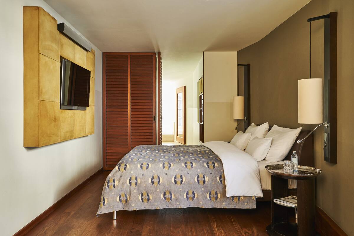A hotel room with a large bed, a TV mounted on the wall, a bedside table with a lamp, and a wooden wardrobe.