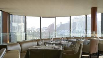A restaurant with tables set for dining, large windows, and a view of the cityscape.