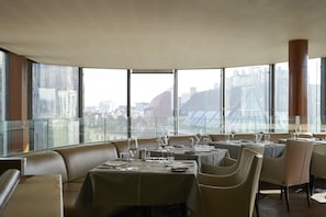 Un restaurante con mesas dispuestas para comer, ventanas amplias y vistas de la ciudad.