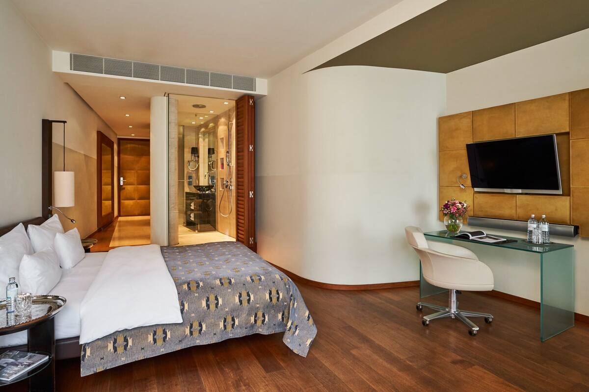 A modern hotel room with a large bed, a glass desk, a TV, and a shower area.