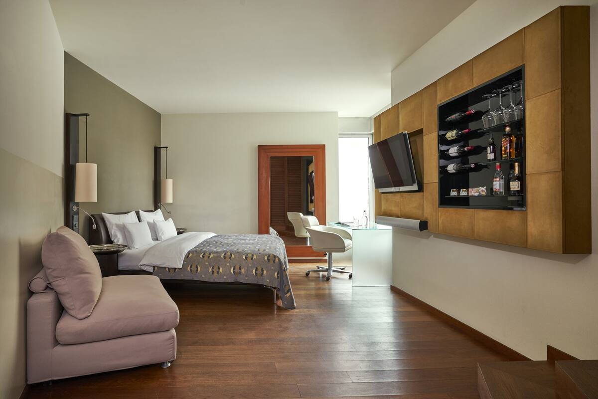A modern hotel room with a bed, a sofa, a desk, and a mounted TV.