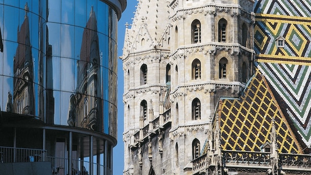 A modern building with a curved glass facade and a traditional building with ornate spires and patterned roof tiles. - DO & CO Hotel Vienna (Vienna)