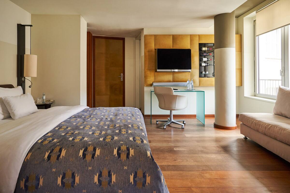 A hotel room with a bed, a desk with a chair, a TV, and a sofa.