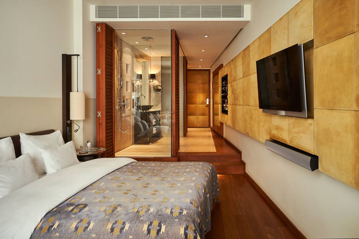 A modern hotel room with a large bed, a TV mounted on the wall, and a walk-in closet with a mirror and vanity.