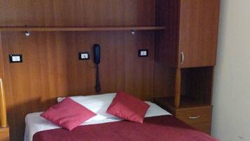 Ein Bett mit roter Decke, ein Holzkopfbrett mit integrierter Beleuchtung und ein kleiner Nachttisch.