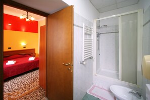 Habitación de hotel con cama roja, puerta de madera, baño con bañera y lavamanos.