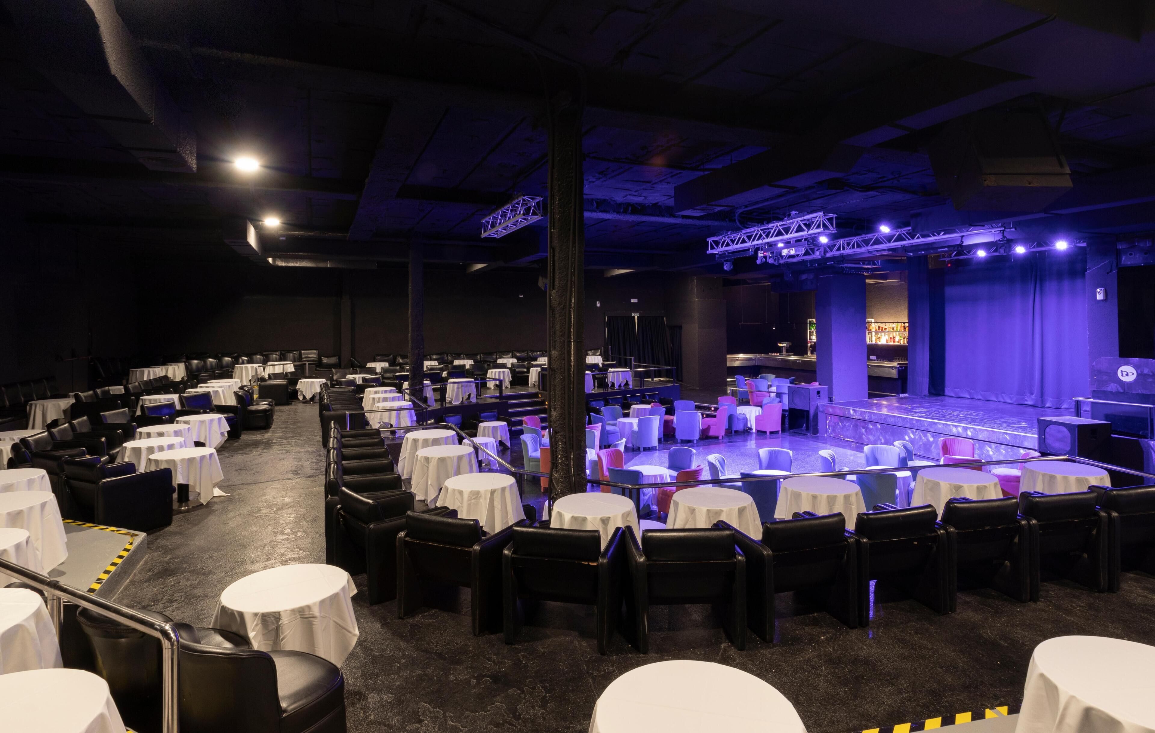 A banquet hall with round tables, chairs, and a stage with lighting.