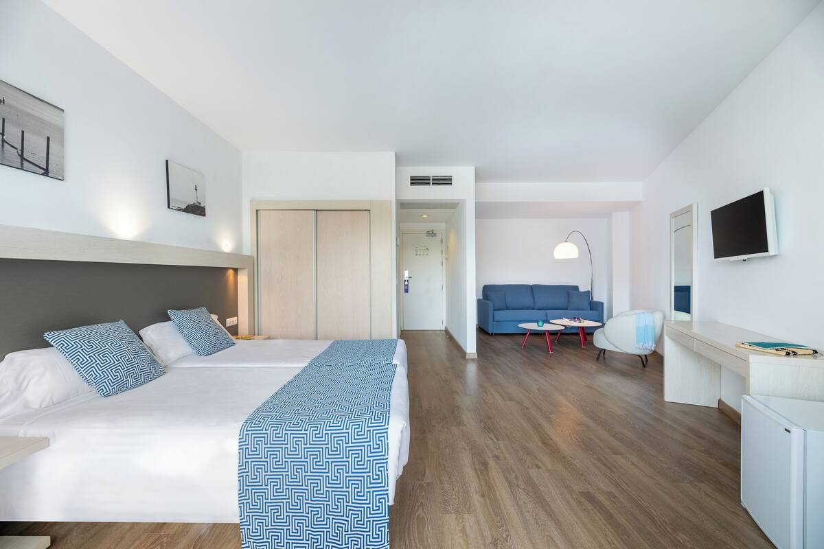 A hotel room with a bed, a desk, a chair, a sofa, and a TV.
